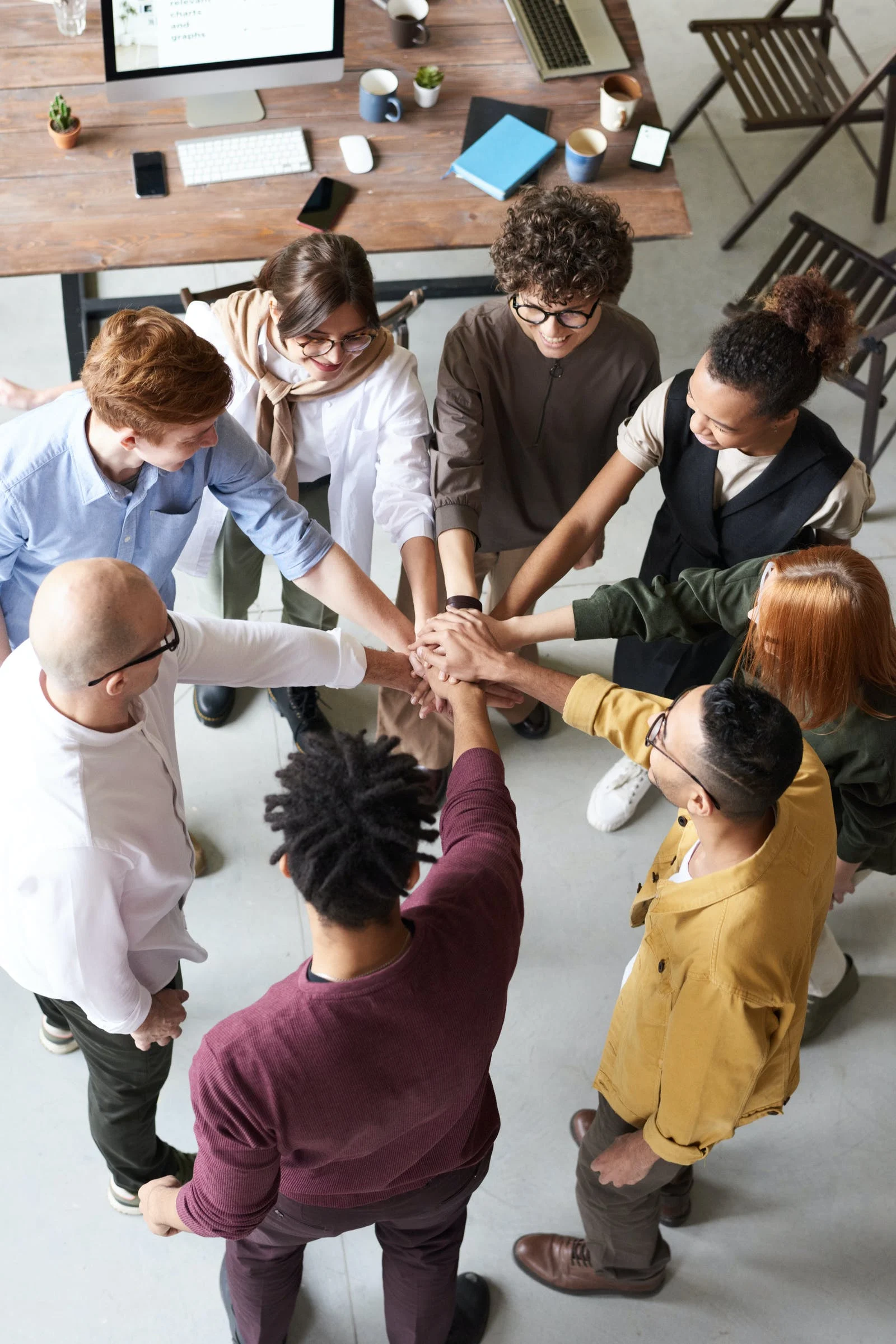 A diverse circle of people each with one hand layered upon other hands in the middle